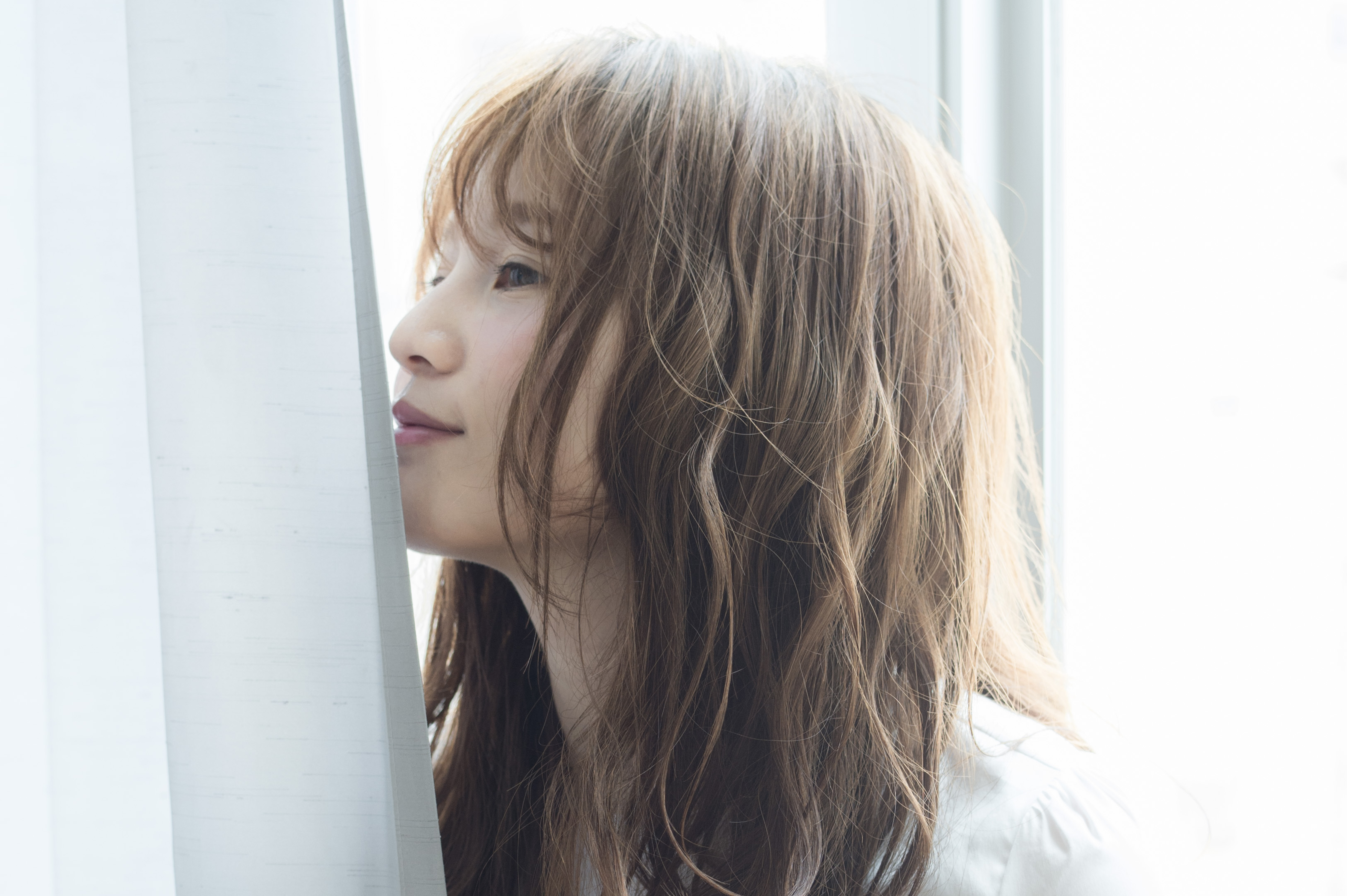 窓辺で大人髪の自然なツヤと質感を見せる女性のイメージ